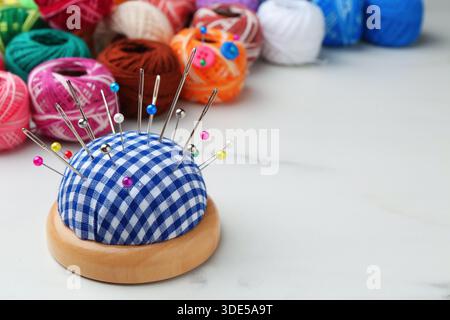 Cuscinetto con aghi e perni sul tavolo bianco, primo piano. Spazio per il testo Foto Stock