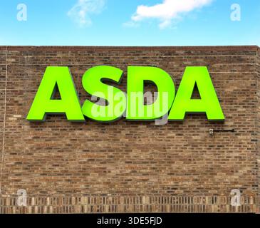 Insegna verde brillante ASDA su una parete di mattoni marrone che rappresenta l'esterno di una catena di supermercati con sede nel Regno Unito, contro un cielo limpido Foto Stock