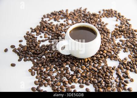 Una tazza di caffè posta su una superficie con chicchi di caffè sparsi intorno. La composizione mette in risalto le ricche tonalità di marrone e l'aroma di pasta fresca Foto Stock