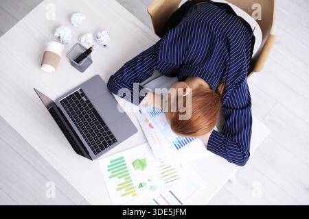 Donna stanca che dorme sul posto di lavoro in ufficio, vista dall'alto Foto Stock