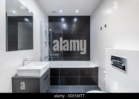 Un bagno contemporaneo con pareti piastrellate nere, vasca, lavabo ed elementi di stile minimalista per un aspetto elegante ed elegante Foto Stock