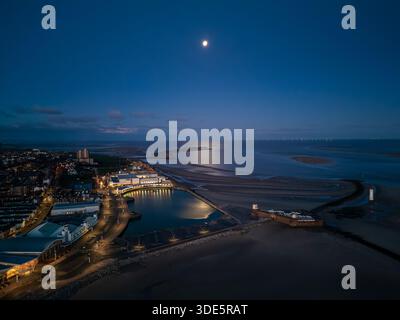 Una vista aerea cattura il paesaggio della luna piena sul lago marino di New Brighton e sul Mare d'Irlanda, Wirral, Regno Unito, all'alba. Foto Stock