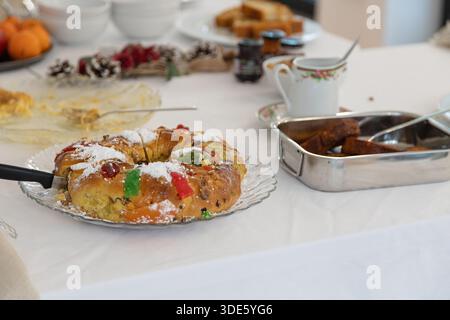 Un tavolo bianco è allestito con tradizionali dolci natalizi, con una torta a fette con frutta candita, toast alla francese, mandarini freschi e mele Foto Stock