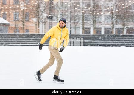 Uomo barbuto di mezza età sulla pista di pattinaggio su ghiaccio, all'aperto nelle giornate invernali innevate Foto Stock