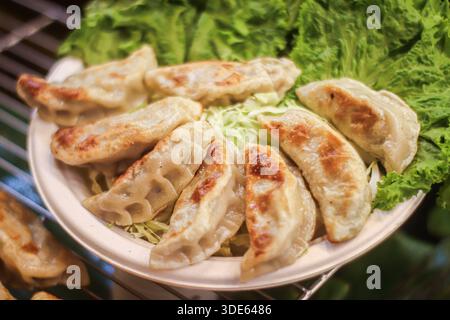Gyoza fritti in padella su foglia di lattuga fresca. Antipasto asiatico croccante e marrone dorato e popolare snack di Street food per uso commerciale. Foto Stock