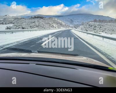 Foto scattata dal sedile del passeggero che mostra un'autostrada parzialmente coperta di neve dopo una tempesta. Parte della strada appare sgombra, con cielo blu e basso c Foto Stock