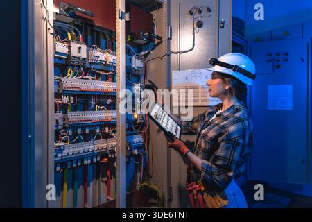 L'elettricista lavora con gruppi di comando industriali e tablet. Ispezione digitale. Foto Stock