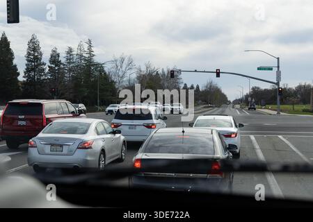 Le auto vengono fermate a un semaforo rosso su una strada suburbana. La scena mostra più veicoli in attesa di procedere. Il cielo è nuvoloso e coperto. Foto Stock