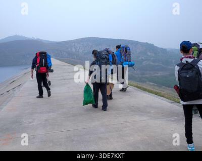 WUHAN, PROVINCIA DI HUBEI, CINA - 31 OTTOBRE 2014: Vista posteriore degli appassionati di attività all'aperto con zaini pesanti che camminano attraverso una diga di cemento nel bacino idrico della L Foto Stock