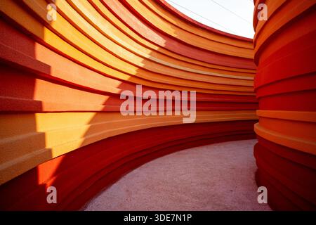 Abstract architectural detail of a curved wall design with layered orange and red panels. The image conveys creativity, modern art, and fluid motion. Foto Stock