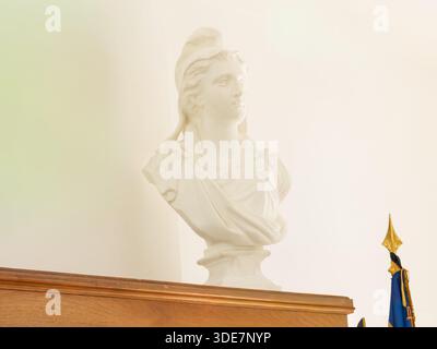 Busto classico in marmo bianco di una figura femminile drappeggiata ispirata all'antica arte greca e romana, esposto all'interno su un morbido sfondo minimalista. Foto Stock