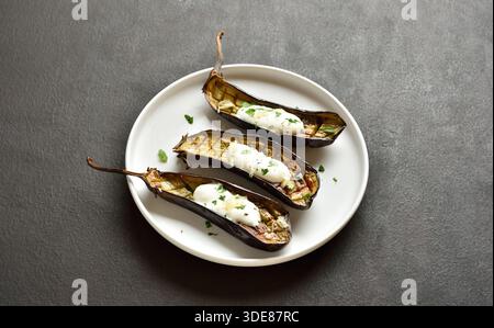 Melanzane al forno con salsa di yogurt all'aglio sul piatto su fondo marrone scuro. Foto Stock