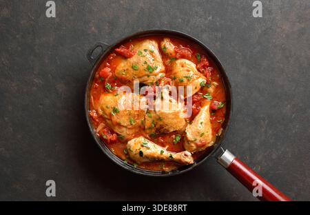 Stufato di pollo georgiano con pomodori ed erbe (chakhokhbili) in padella di ghisa su fondo di pietra scura. Pollo al forno con sugo di verdure al pomodoro. Foto Stock