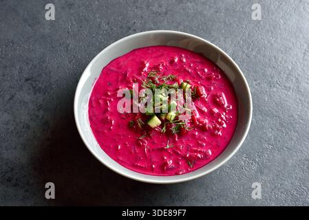 Zuppa di panna di barbabietola con yogurt, cetriolo e aneto nel recipiente su sfondo blu. Zuppa fredda estiva. Vista ravvicinata Foto Stock