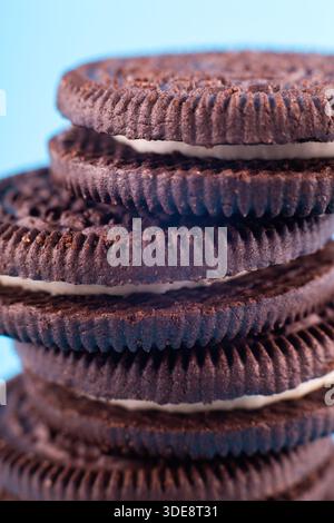 biscotti al cioccolato sandwich nero macro brown con crema di latte bianca su sfondo blu. Concetto delizioso e gustoso Foto Stock