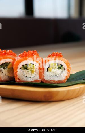 Tre panini di sushi ripieni di salmone, cetriolo e avocado sono disposti ordinatamente su un vassoio di legno Pesce fresco e ingredienti colorati esaltano il Ja Foto Stock