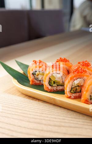 I colorati sushi roll con ingredienti freschi sono disposti ordinatamente su un piatto di legno. I panini includono salmone, verdure e uova di pesce d'arancia, pronti per Foto Stock