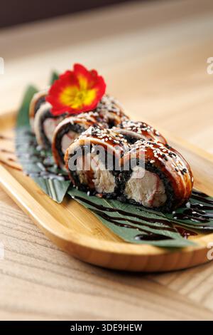 Gli involtini di sushi sono disposti ordinatamente su un piatto di bambù. Il piatto presenta riso nero, pesce e una decorazione floreale. Servito in un dini informale Foto Stock