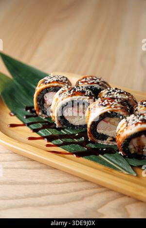 Panini di sushi freschi seduti su un piatto di legno con foglie di bambù. Il piatto presenta vari ripieni e condimenti, mostrando la variegata cucina giapponese Foto Stock