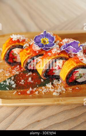 I colorati sushi roll sono disposti ordinatamente su un piatto di legno. I panini sono caratterizzati da strati di pesce e verdure condite con fiori e spezie commestibili. Foto Stock