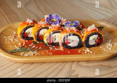 Un piatto di legno mostra vibranti sushi panini ripieni di vari ingredienti. I fiori commestibili e i condimenti aggiungono colore e consistenza al piatto. Questo piatto Foto Stock