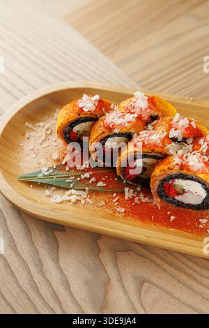 I colorati sushi roll sono disposti su un piatto di legno. I panini contengono ingredienti come riso, verdure e pesce ricoperti di trucioli e spezie. Foto Stock