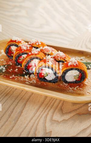 Un piatto di legno mostra diversi panini di sushi vivaci ripieni di verdure e formaggio spalmabile, guarniti con guarnizioni. Il piatto è disposto in modo ordinato Foto Stock