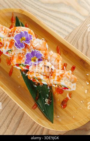 Panini di sushi ripieni di ingredienti freschi e ricoperti di gamberetti su un piatto di bambù. Il piatto presenta colori vivaci ed è guarnito con commestibile Foto Stock