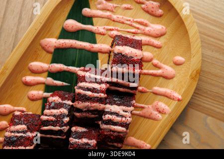 Il piatto mostra sushi roll disposti ordinatamente su un piatto di bambù. I panini sono ricoperti da una vivace salsa rosa e guarniti con una foglia verde. La S Foto Stock
