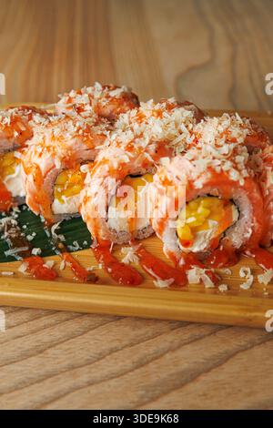 Un piatto di sushi presenta diversi panini conditi con salmone e scaglie croccanti. I panini contengono mango e formaggio spalmabile, serviti su una tavola di legno. Foto Stock