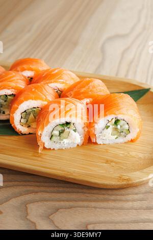 Una tavola di legno presenta dei sushi freschi preparati con salmone e cetriolo. Questo piatto mostra l'arte della cucina giapponese, pronta per essere gustata per il pranzo Foto Stock