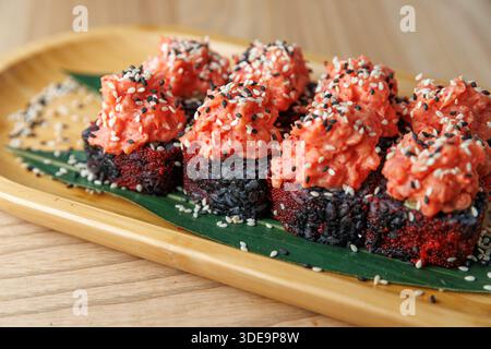 Gli involtini di sushi si siedono su un piatto di bambù con pesce rosso e semi di sesamo nero. L'ambiente e' informale e invitante, tipico di un'esperienza culinaria Giapponese. Foto Stock