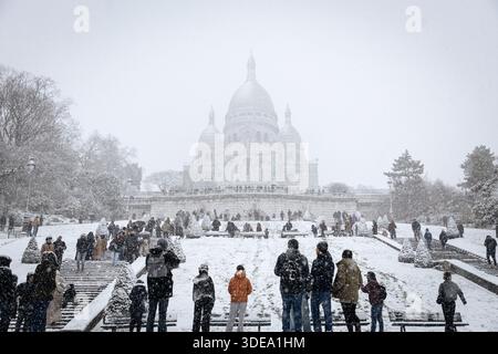 La basilica del Sacro cuore di Montmartre è visibile durante la forte tempesta di neve che ha colpito Parigi. Una forte tempesta di neve ha colpito la capitale francese, causando molta eccitazione tra parigini e turisti , ma anche un sacco di disagi nei trasporti su strada. Vicino alla Basilica del Sacro cuore nel quartiere di Montmartre, la gente scivola giù dalla collina sulla neve. Foto Stock