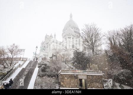 La basilica del Sacro cuore di Montmartre è visibile durante la forte tempesta di neve che ha colpito Parigi. Una forte tempesta di neve ha colpito la capitale francese, causando molta eccitazione tra parigini e turisti , ma anche un sacco di disagi nei trasporti su strada. Vicino alla Basilica del Sacro cuore nel quartiere di Montmartre, la gente scivola giù dalla collina sulla neve. Foto Stock