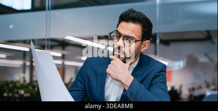 Man legge i documenti in un ufficio moderno durante l'orario di lavoro mentre pensa Foto Stock