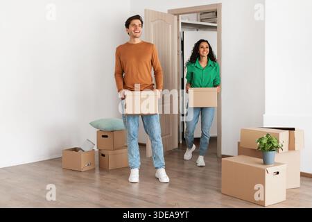 Coppia felice che esplora la loro nuova casa mentre trasporta scatole di cartone Foto Stock