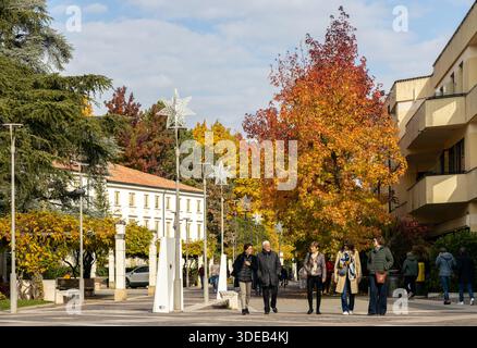 Abano Terme, Italia - 29 ottobre 2025: Persone che camminano lungo una strada alberata con fogliame autunnale nel centro del paese Foto Stock