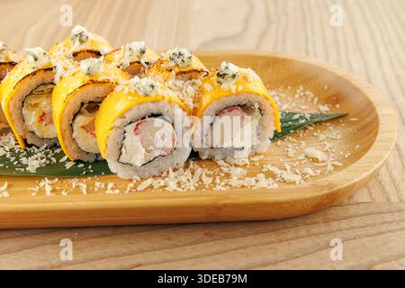 Un piatto propone sushi roll preparati in modo ordinato. I panini sono ricoperti di formaggio grattugiato e posti su una foglia verde, evidenziandone i colori Foto Stock