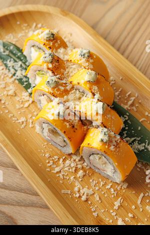 Gli involtini di sushi sono disposti ordinatamente su un piatto di legno. I panini sono ricoperti da una decorazione saporita e presentati con cura per i dettagli. Foto Stock