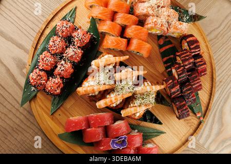 Un vassoio di legno mostra un assortimento di sushi, tra cui panini ripieni di pesce fresco, gamberi e condimenti colorati. I piatti sono disposti in verde Foto Stock