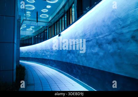 Vista notturna di un percorso urbano curvo illuminato da luci LED blu neon e soffitto circolare, creando un'atmosfera futuristica da tunnel fantascientifico Foto Stock