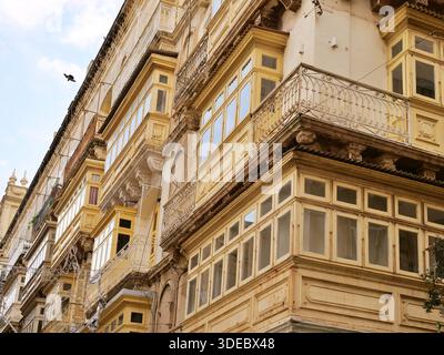 Tradizionali balconi in legno giallo sullo storico edificio in pietra calcarea a la Valletta Malta, con vista ad angolo basso della classica architettura mediterranea nella città vecchia Foto Stock