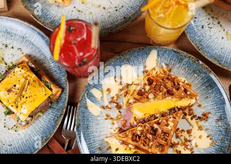 Vari piatti sono disposti su piatti. Il tavolo offre waffle conditi con ingredienti, accompagnati da bevande colorate, per creare un ambiente dal vivo Foto Stock