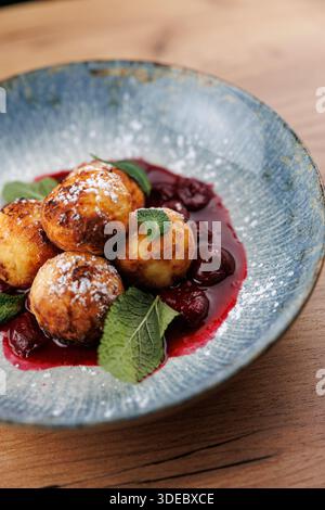 I gnocchi sono disposti in una ciotola con una vivace salsa di frutti di bosco e guarniti con foglie di menta fresca. Il piatto mostra i sapori tradizionali ucraini Foto Stock