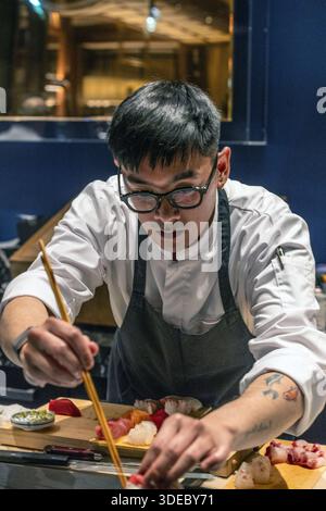 Lo chef sushi prepara meticolosamente sashimi freschi al sushi bar in un esclusivo ristorante giapponese. Foto Stock