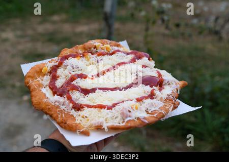 Viaggia in romania transilvania targu mures con in mano un lángos, un tradizionale impasto fritto ungherese, condito con formaggio e ketchup Foto Stock