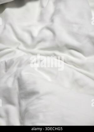 Il morbido sfondo bianco in tessuto mostra lenzuola rugose piegate con un materiale di cotone pulito e luminoso per una confortevole sensazione di intimità Foto Stock