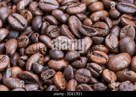 I chicchi di caffè espresso scuri con messa a fuoco ravvicinata rivelano una lucentezza oleosa e colori profondi, l'illuminazione ad alto contrasto enfatizza la consistenza densa e la superficie arrostita, intens Foto Stock