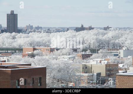 Un paesaggio urbano invernale illuminato dal sole, dove gli edifici residenziali lasciano il posto a una lontana foresta di alberi scintillanti con neve pesante e ghiaccio sotto il limpido Foto Stock