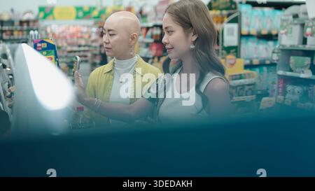 Due donne asiatiche che selezionano i prodotti nel negozio di alimentari, una che utilizza lo smartphone per la scansione Foto Stock